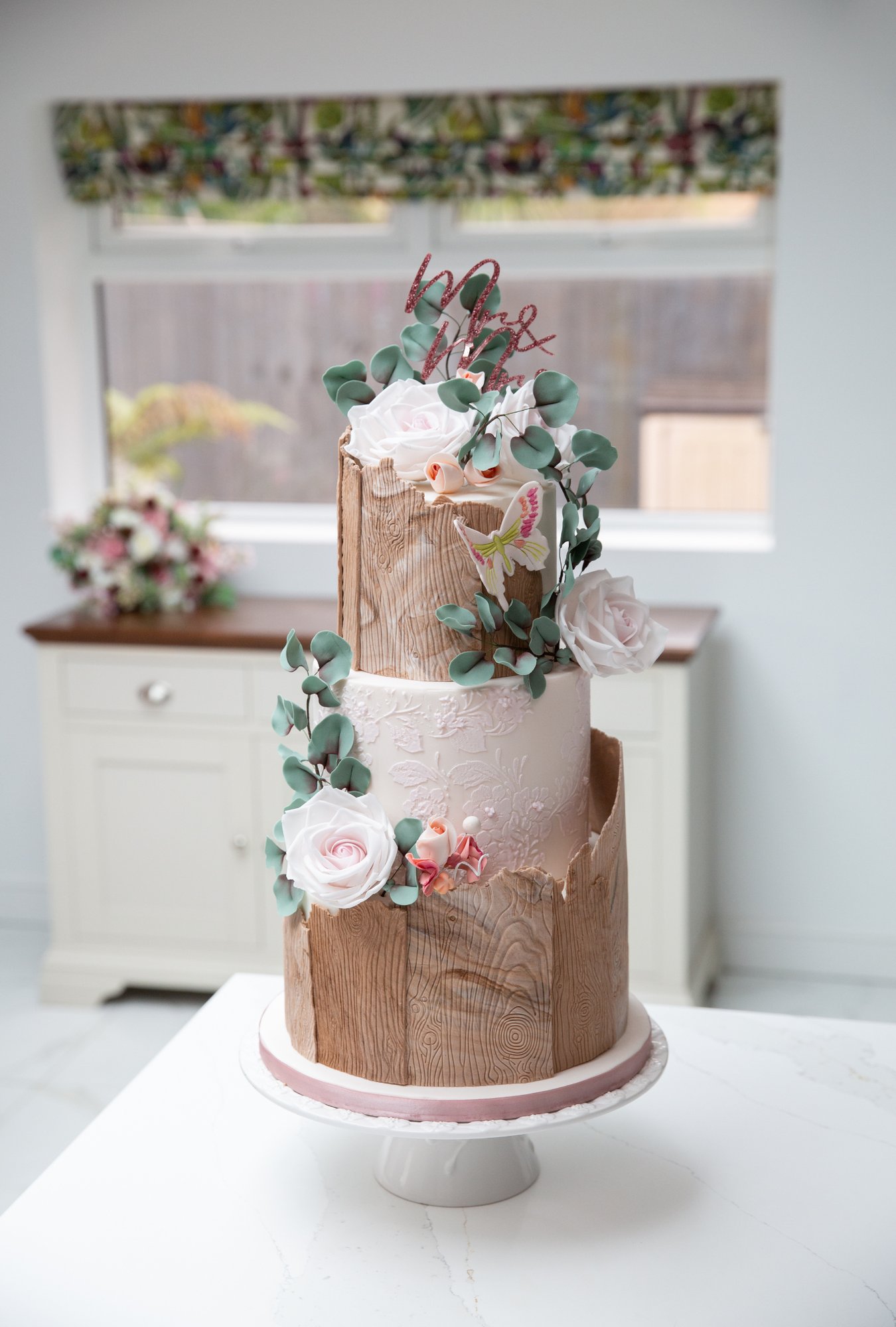 Three tier brown and cream wedding cake topped with fresh flowers and a Mr & Mrs monogram cake topper