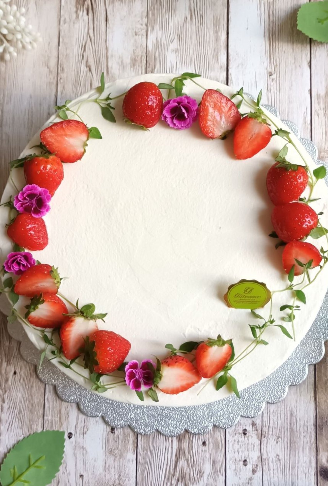 A large round cake with a white buttercream icing decorated with a ring of strawberries and wildflowers