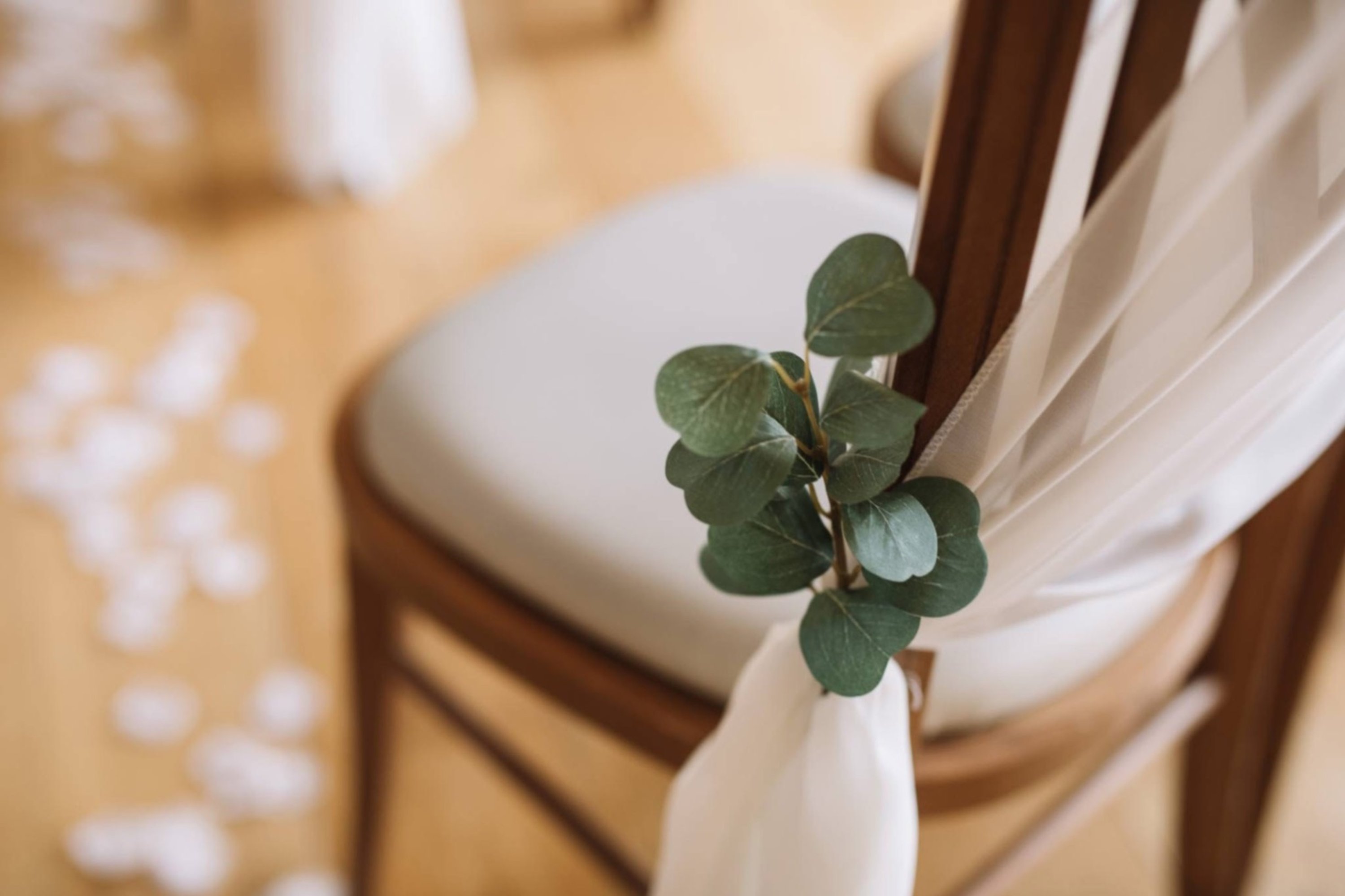 sprig of dried eucalyptus tied to a chair in a long white aisle