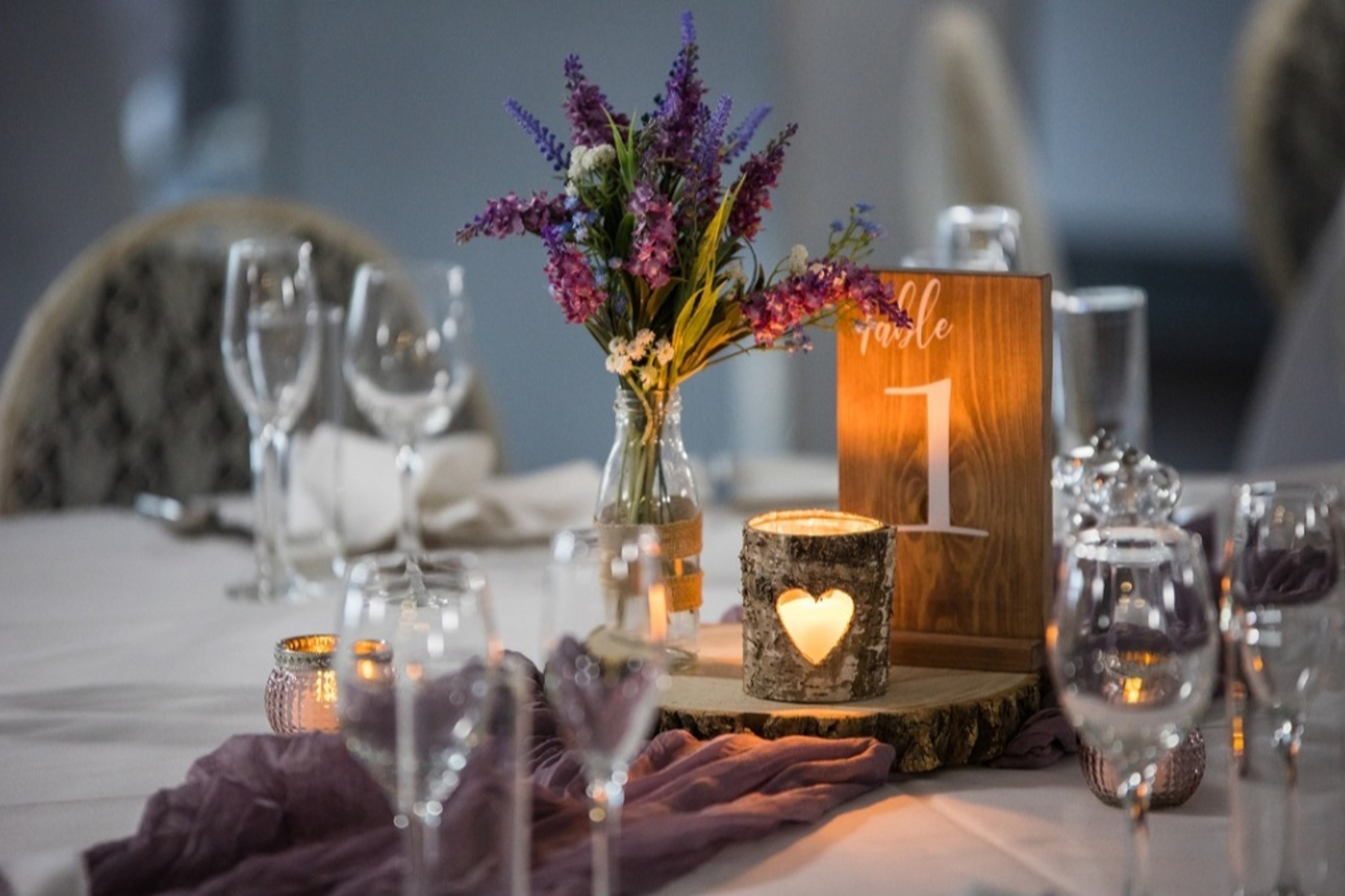 rustic wooden table number on a boho woodland themed table with a heart tealight and glassware amongst purple blooms