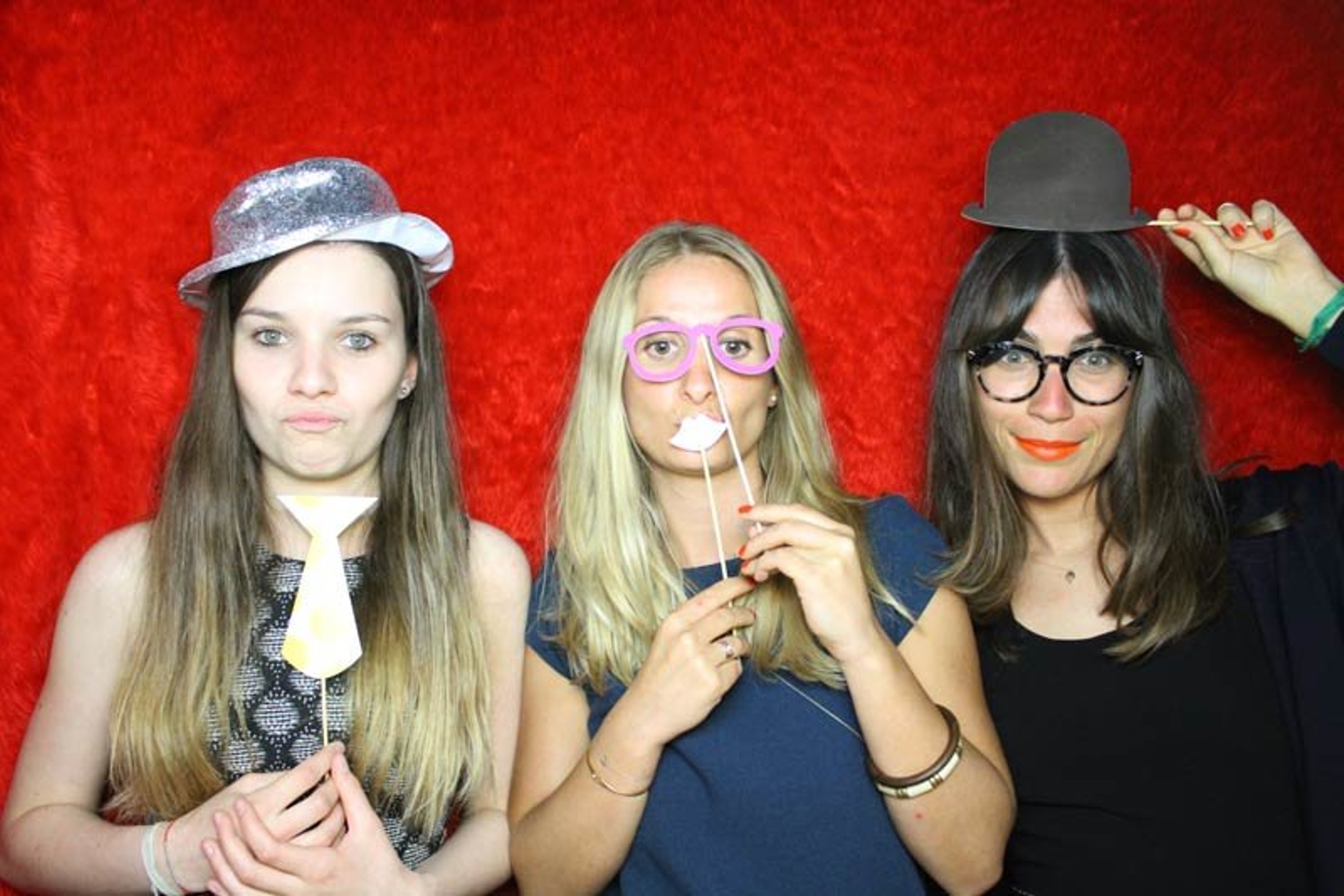 three friends stood in a line using silly props in a photo booth