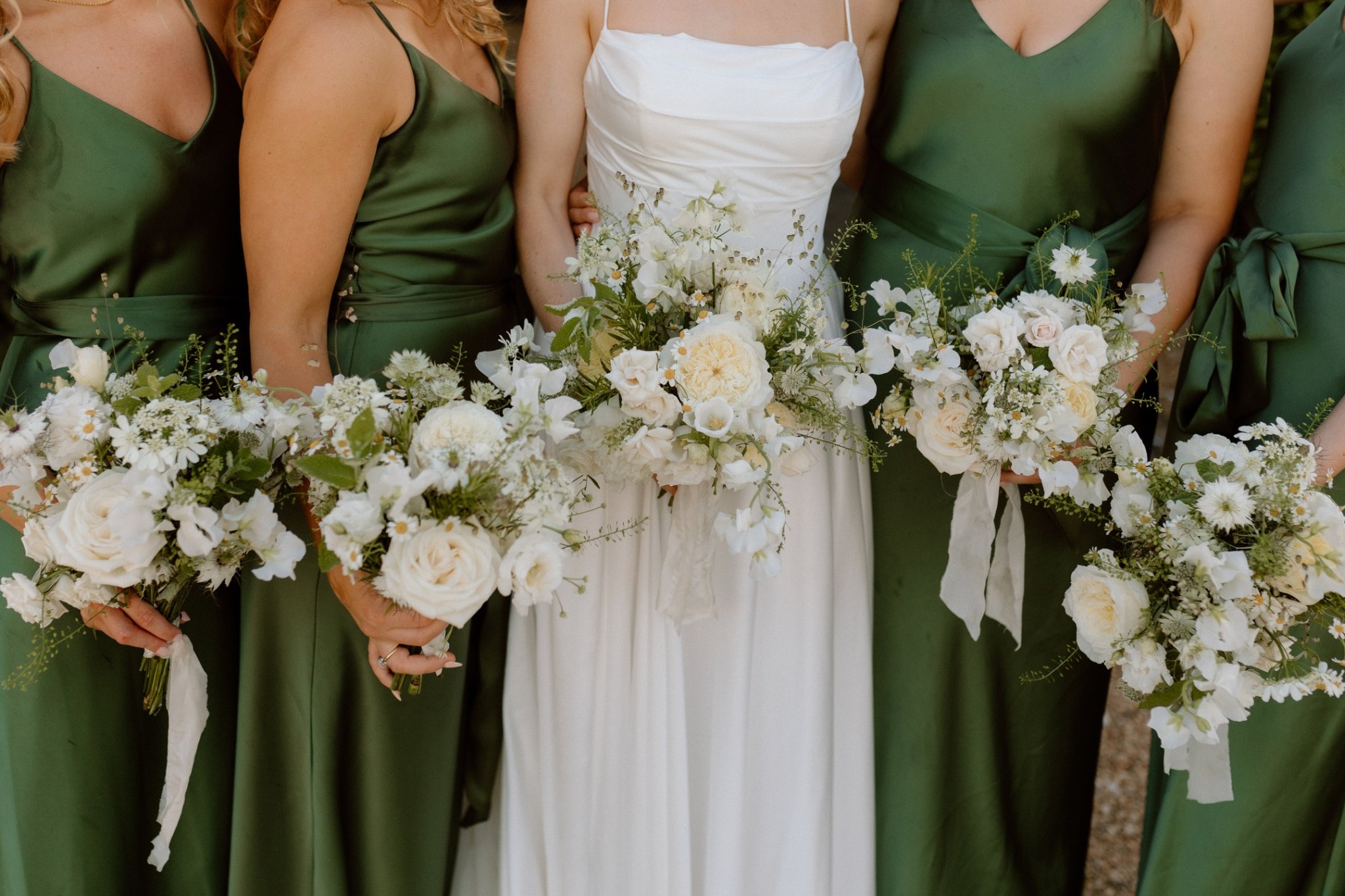 Bride and bridesmaids holding wedding bouquets with greenery