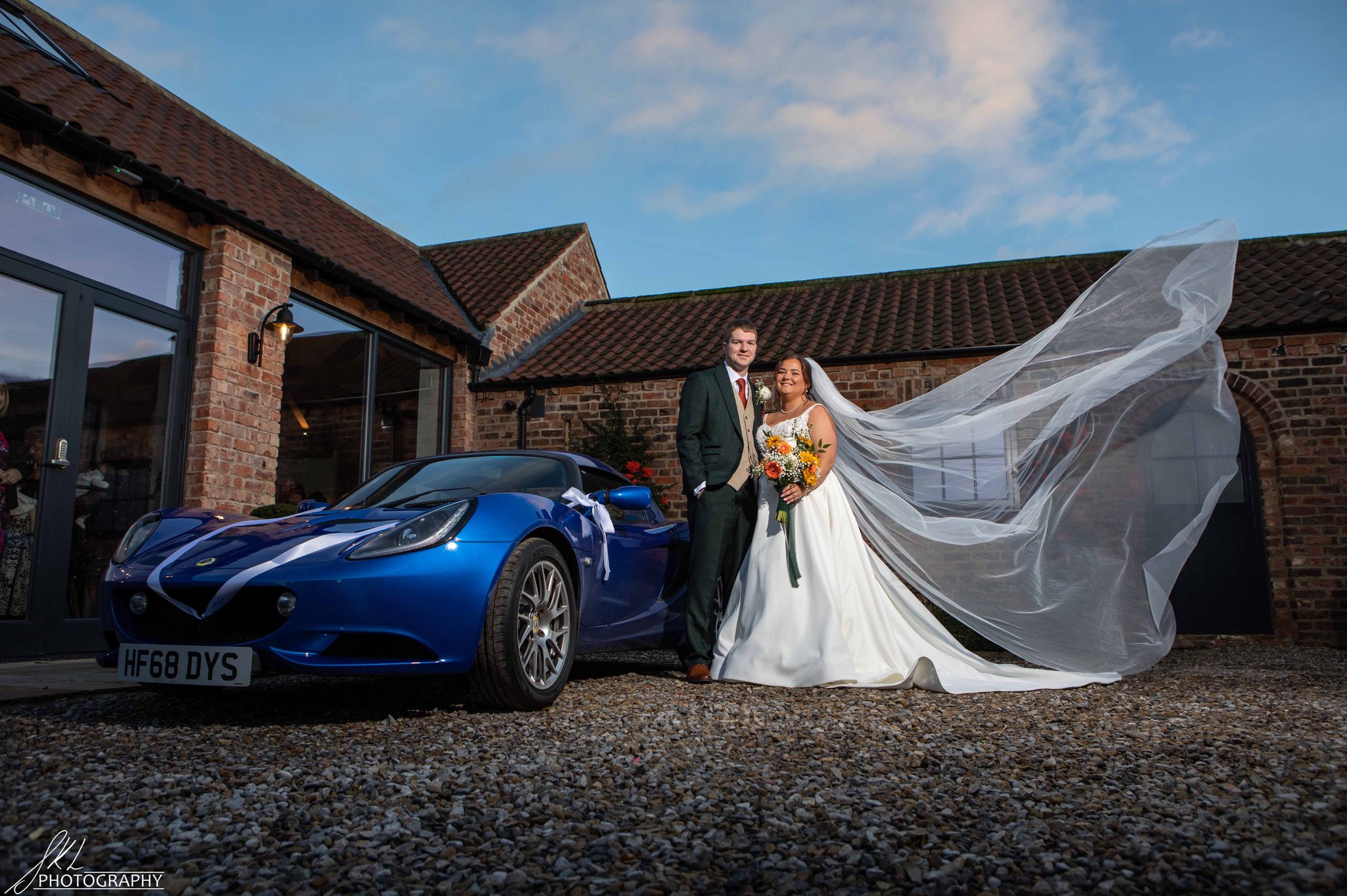 Bride and groom posing for a wedding photo next to a sports car
