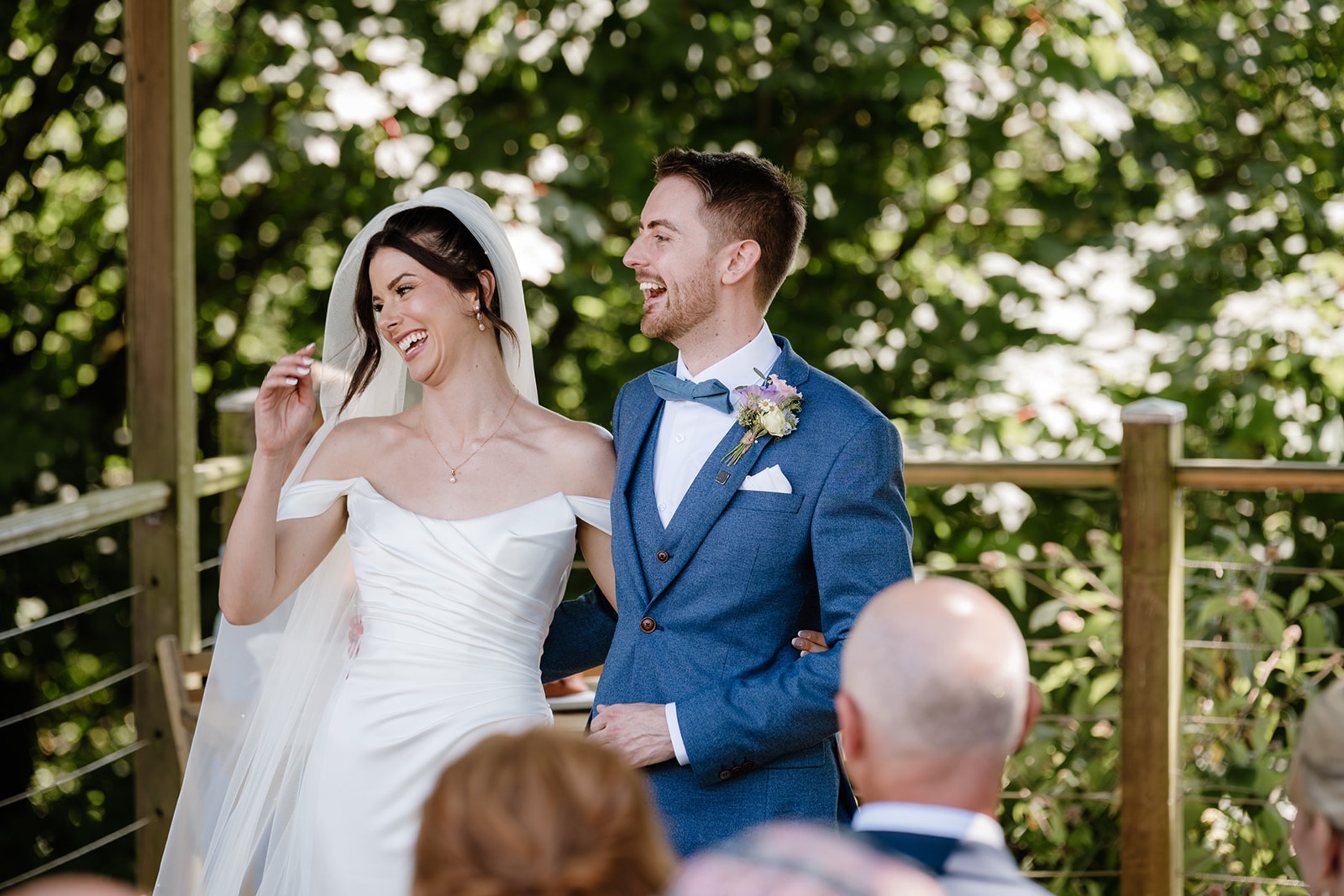 bride and groom laughing standing beneath a gazebo at sunset, embracing and smiling
