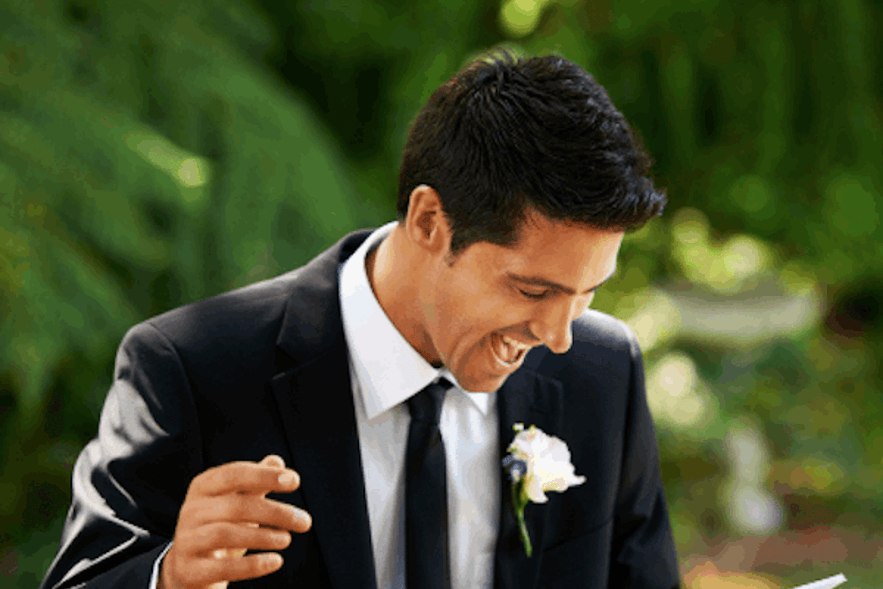 A groom in a black and white suit reading his speech with energy, gesturing to the crowd and laughing