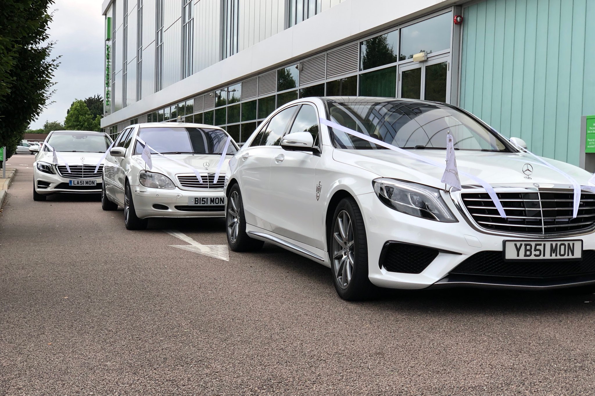 Line of white mercedes wedding cars decorated with ribbons