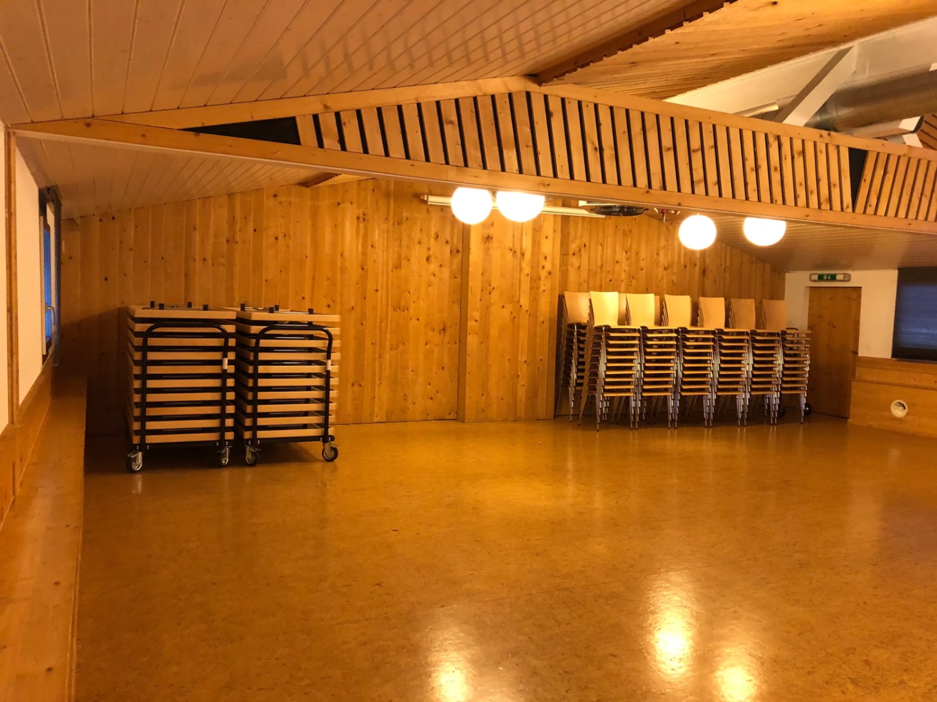 Der leere Saal mit Holzgebälk und gestapelten Stühlen