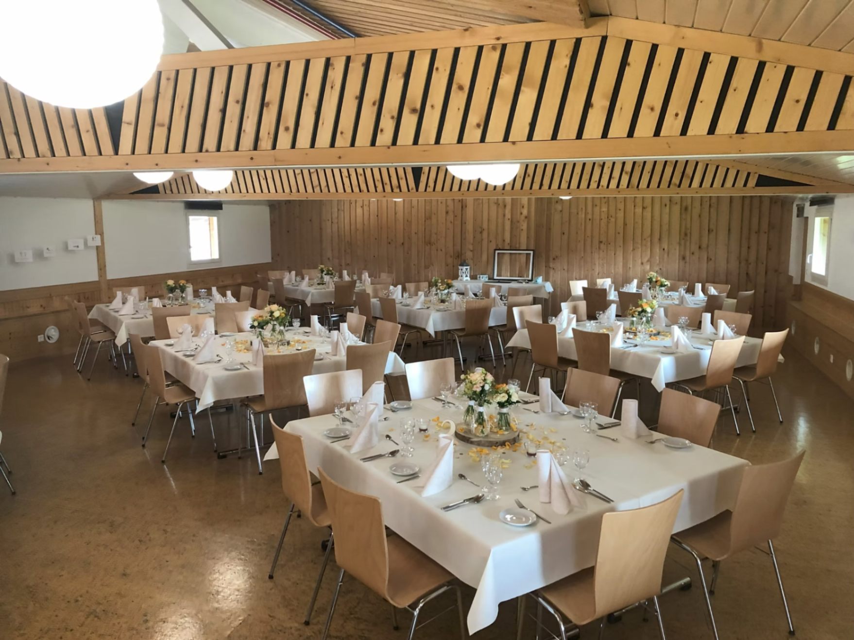 Der Saal mit weiss gedeckten Tischen und Blumenschmuck bei Tageslicht