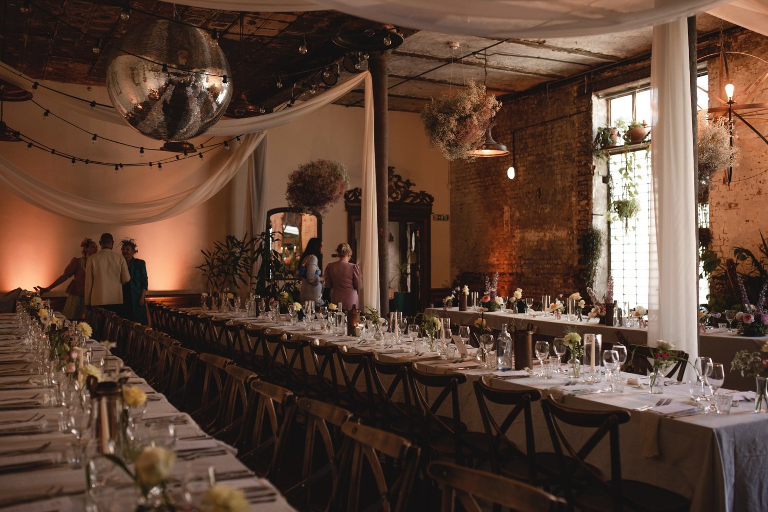 Wedding breakfast indoors with drapery and a disco ball hanging from the ceiling