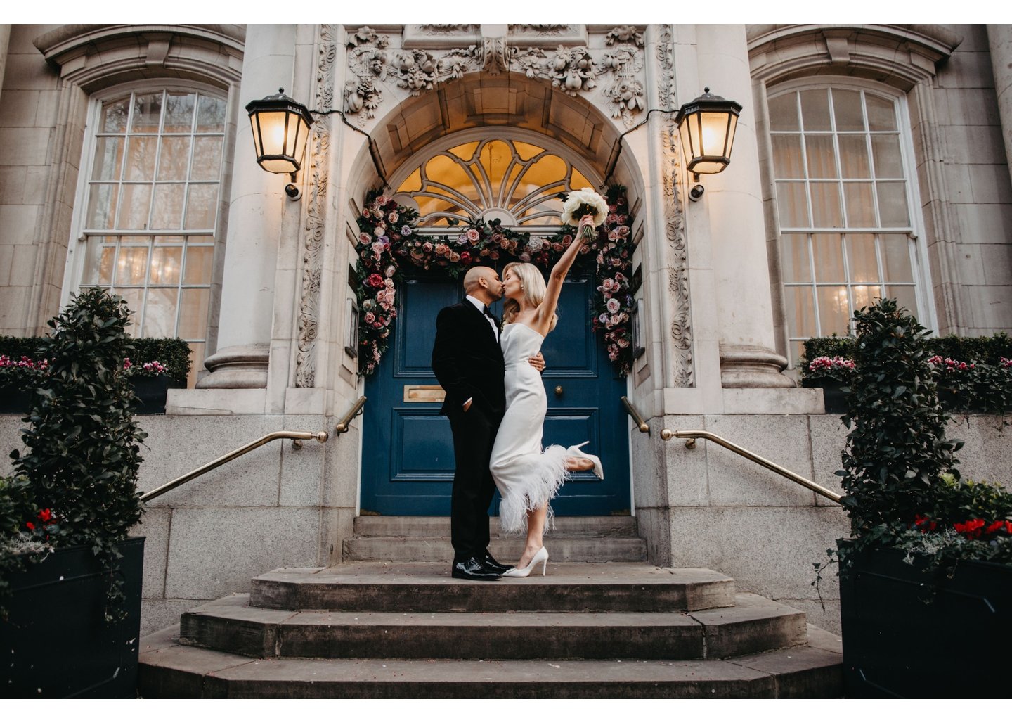 a bride and groom kissing in front of Kensington and Chelsea Register Office on the steps in front of the door, the bride holding a bouquet up to the sky