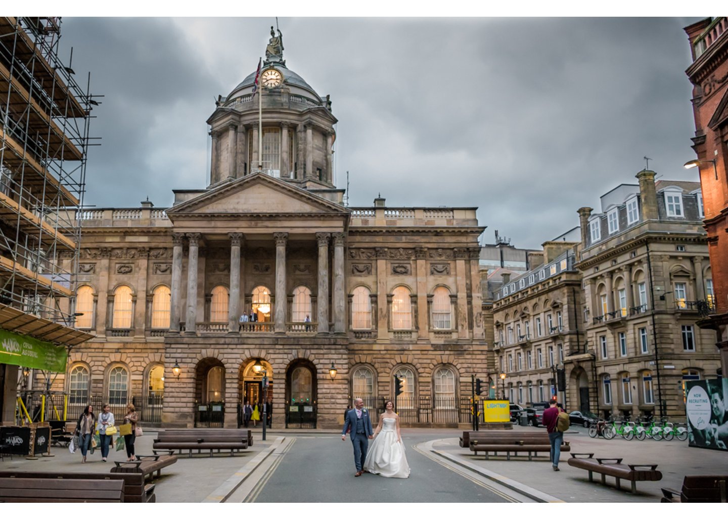 bride and groom holding hands as they walk outside the front of Liverpool Registry Office lit up under the clouds