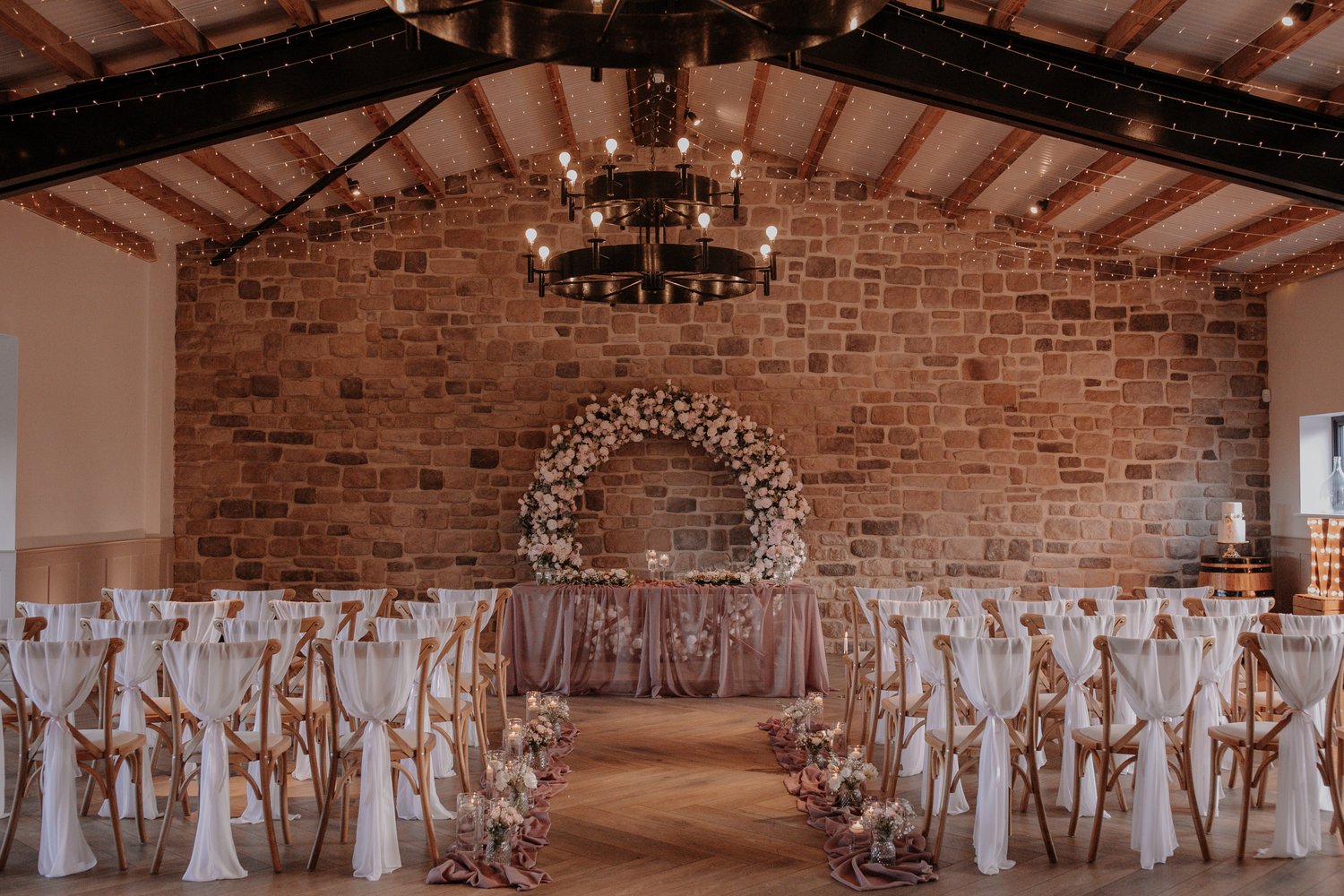 Indoor wedding ceremony set up with brick walls and rustic chandelier hanging from the ceiling