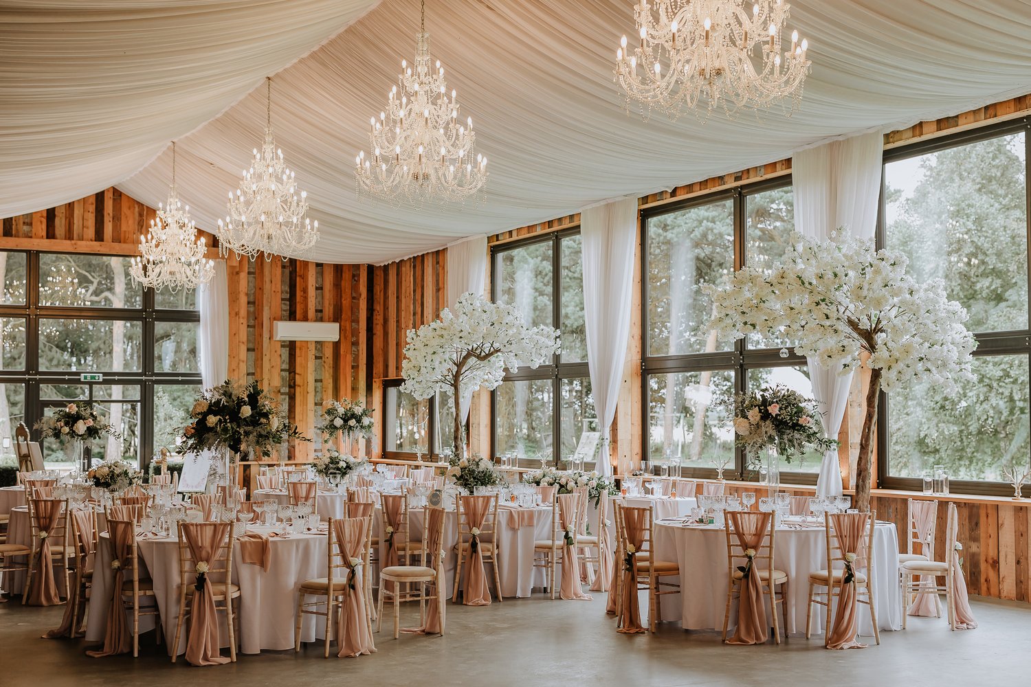 an elegant wedding breakfast set up with drapery and chandeliers hanging from the ceiling