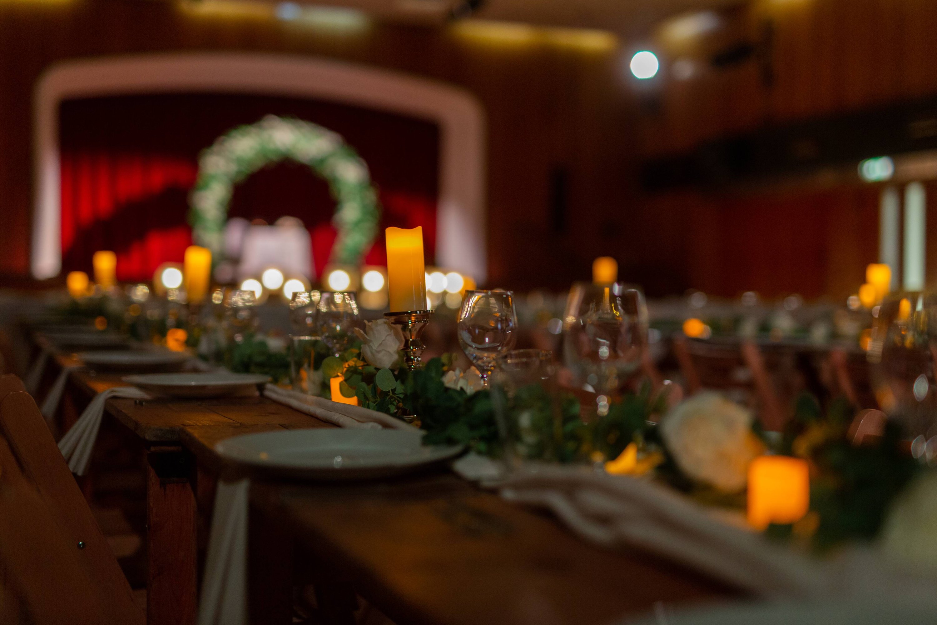 a long table decorated with white roses, greenery and pillar candles lit up in the light in front of an arch