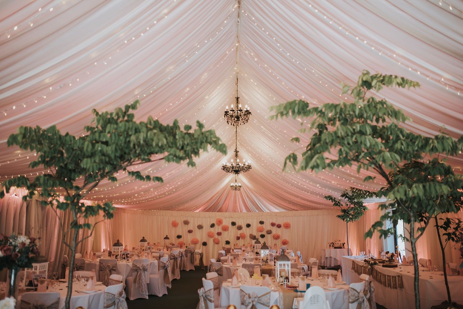 marquee set up for a wedding breakfast featuring chandeliers and foilage 