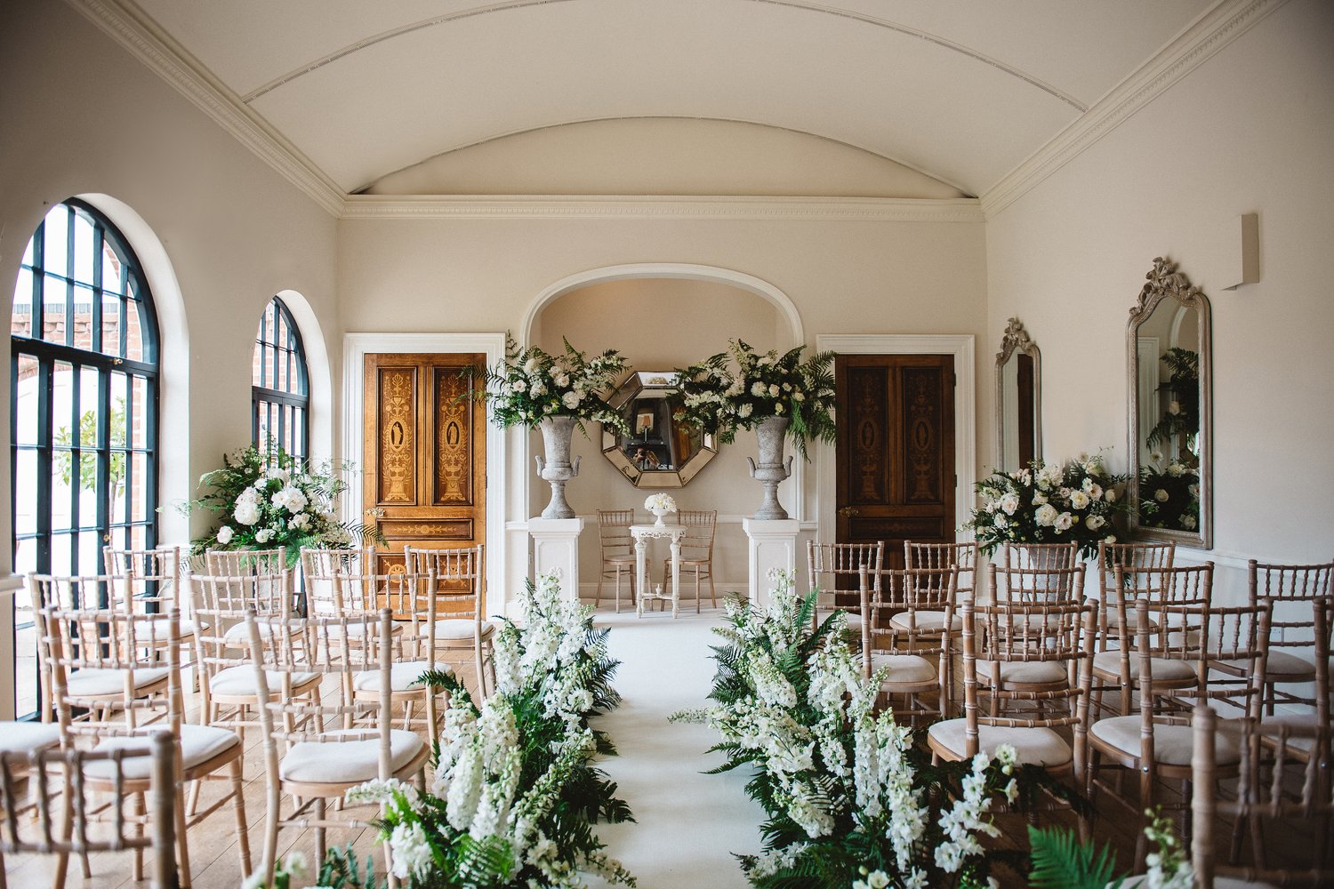 A beautifully set up indoor ceremony with flowers lining the aisle 