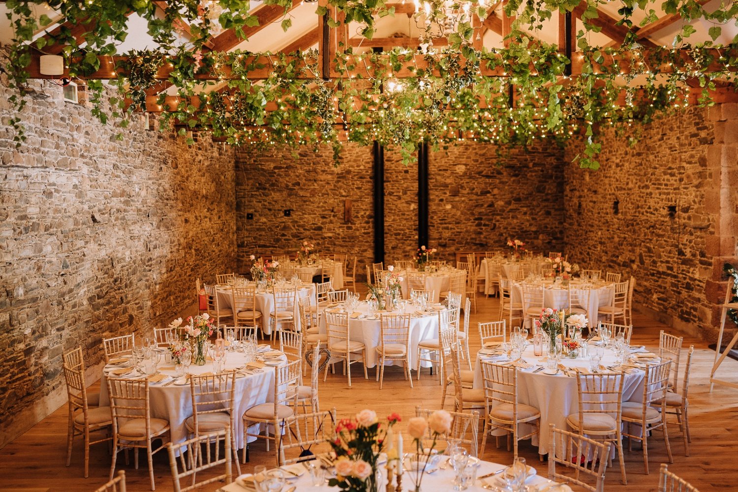 Wedding breakfast set up with wooden beams and draping foilage above 