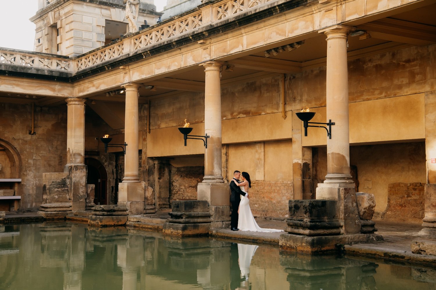 Couple embracing in wedding attire at the Roman Baths in Bath
